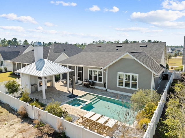 rear view of property featuring outdoor dry bar, a pool with connected hot tub, roof with shingles, a fenced backyard, and a patio area