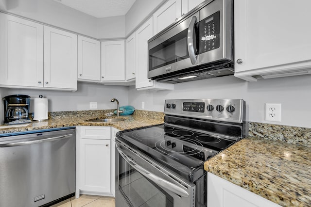 kitchen with light stone countertops, stainless steel appliances, a textured ceiling, white cabinetry, and a sink