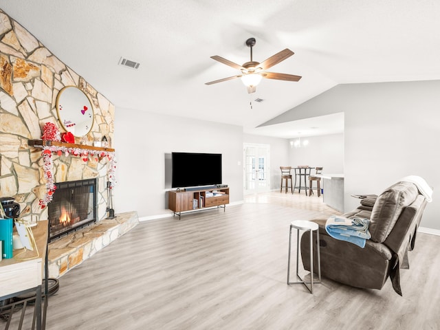 living room with lofted ceiling, a stone fireplace, ceiling fan with notable chandelier, wood finished floors, and visible vents