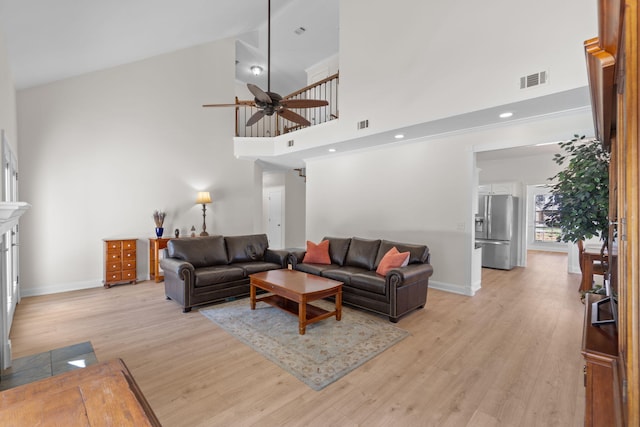 living room featuring light wood finished floors, visible vents, baseboards, a fireplace with flush hearth, and a high ceiling