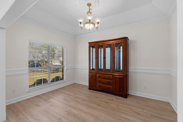 empty room featuring a raised ceiling, light wood-style flooring, baseboards, and an inviting chandelier