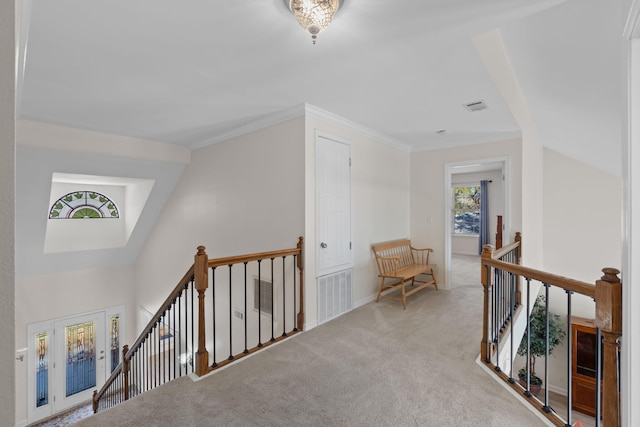 hallway featuring carpet flooring, visible vents, crown molding, and an upstairs landing