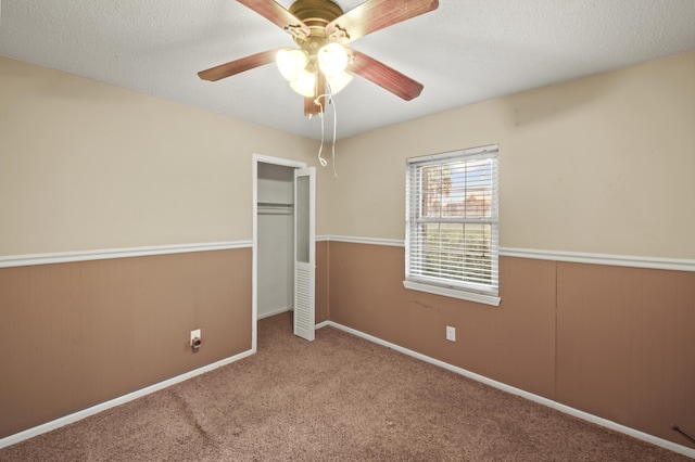 unfurnished bedroom featuring a wainscoted wall, ceiling fan, carpet, a textured ceiling, and a closet