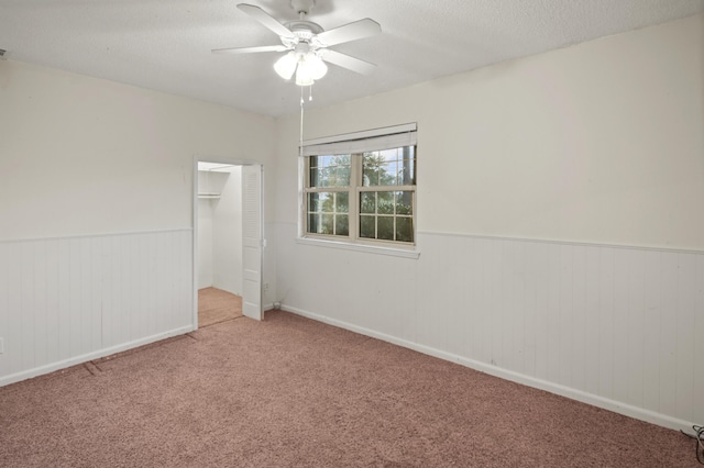 unfurnished bedroom with a closet, wainscoting, carpet flooring, ceiling fan, and a textured ceiling