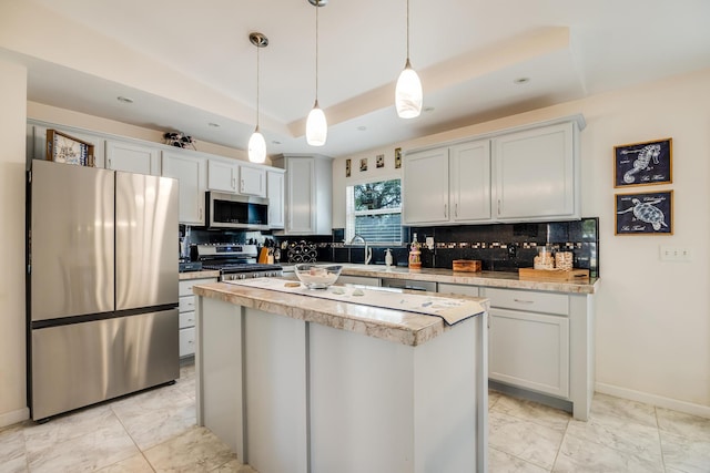 kitchen with stainless steel appliances, hanging light fixtures, light countertops, a tray ceiling, and tasteful backsplash