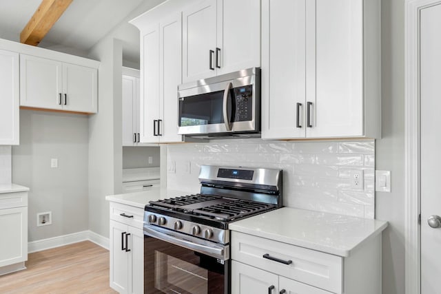 kitchen with appliances with stainless steel finishes, white cabinetry, backsplash, and baseboards