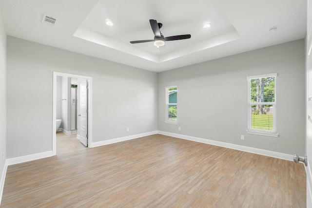 unfurnished room with light wood-type flooring, a tray ceiling, and baseboards