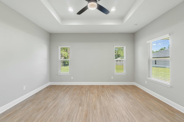 empty room featuring light wood-type flooring, a raised ceiling, and baseboards