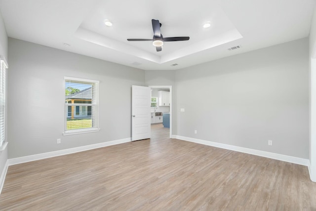 empty room featuring light wood finished floors, baseboards, visible vents, and a raised ceiling