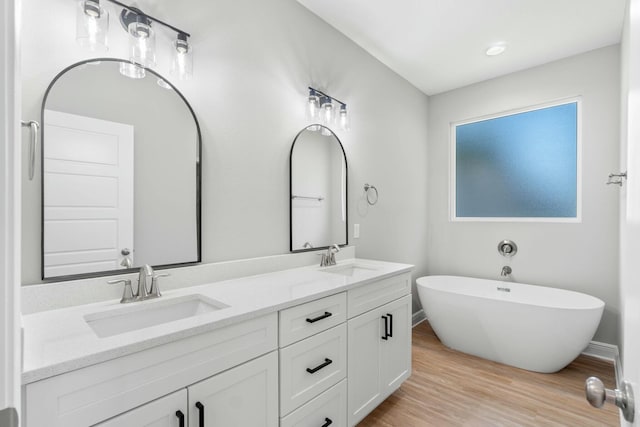 bathroom featuring double vanity, a sink, a freestanding bath, and wood finished floors