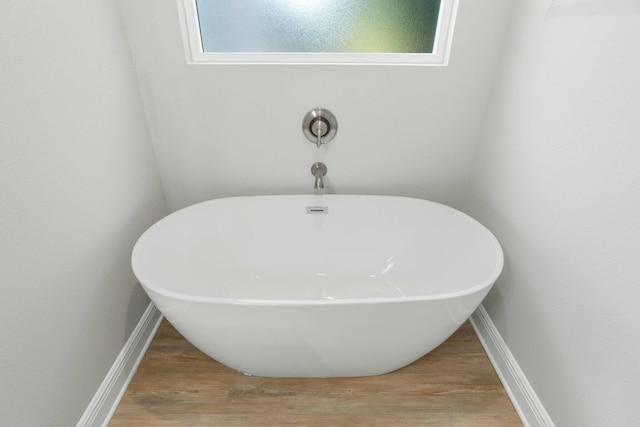 bathroom with a freestanding tub, baseboards, and wood finished floors