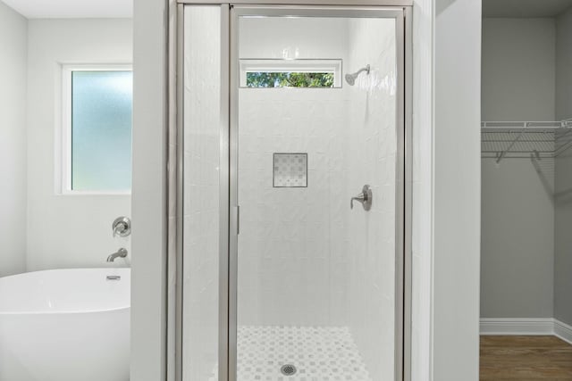 bathroom featuring a stall shower, baseboards, wood finished floors, a walk in closet, and a freestanding tub