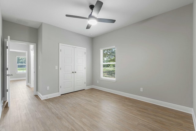 unfurnished bedroom with light wood-style floors, a closet, multiple windows, and baseboards