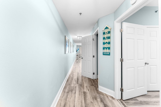 corridor featuring light wood-style flooring and baseboards