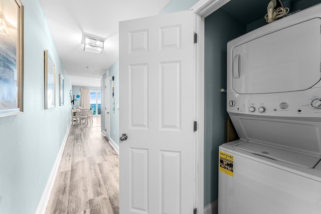 laundry room featuring laundry area, baseboards, light wood-style floors, and stacked washer / dryer