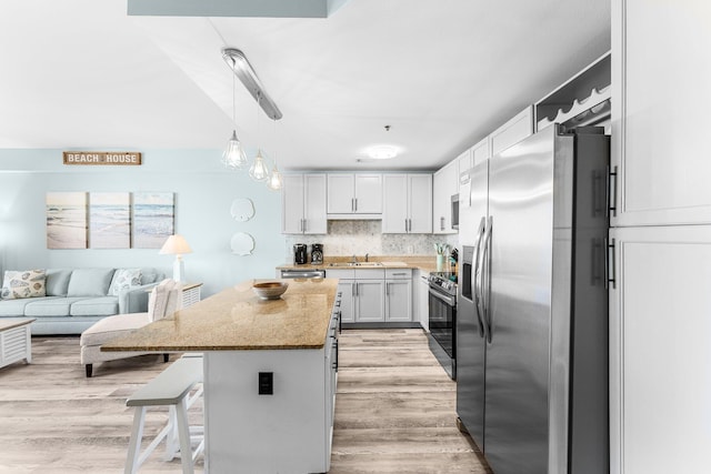 kitchen with a center island, light wood finished floors, stainless steel appliances, tasteful backsplash, and a sink