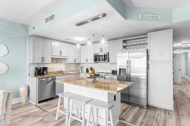 kitchen with open shelves, visible vents, appliances with stainless steel finishes, a sink, and light stone countertops