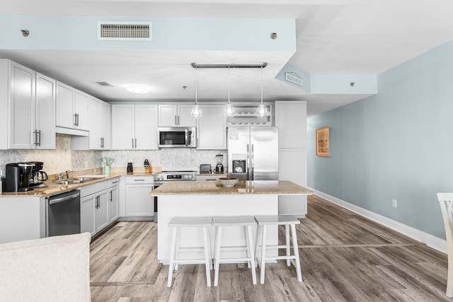 kitchen with visible vents, decorative backsplash, appliances with stainless steel finishes, a kitchen breakfast bar, and a sink