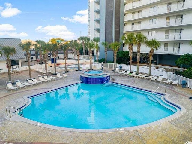 community pool with a hot tub, fence, and a patio