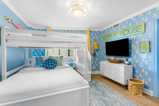 bedroom with ornamental molding, wood finished floors, a textured ceiling, and wallpapered walls