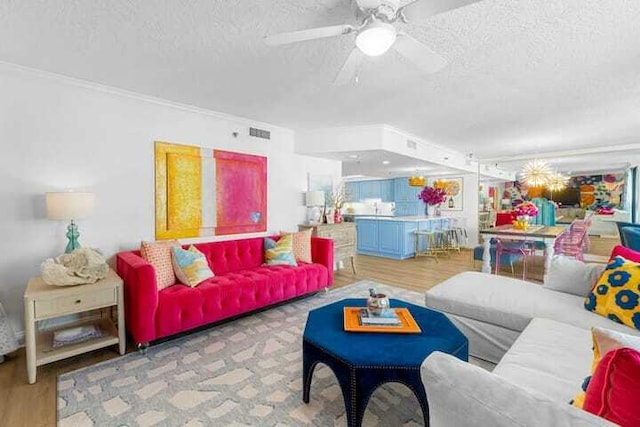 living area with a ceiling fan, visible vents, a textured ceiling, and wood finished floors