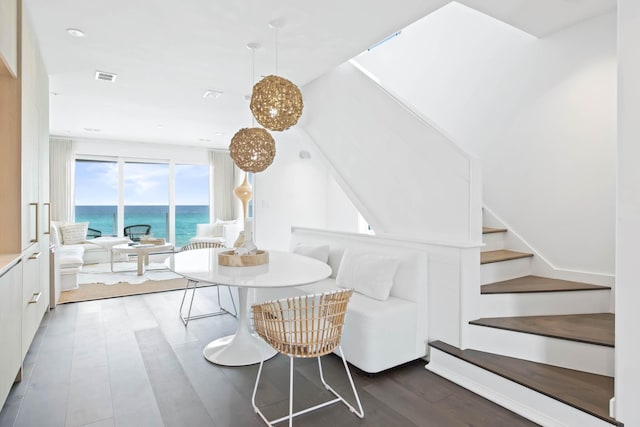 dining area featuring stairway, a water view, wood finished floors, and visible vents