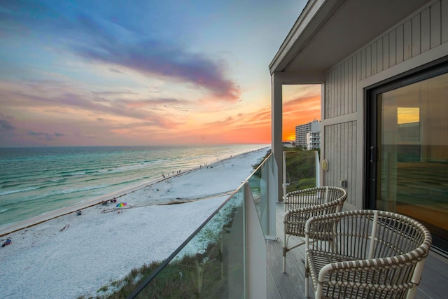 balcony at dusk with a water view and a view of the beach