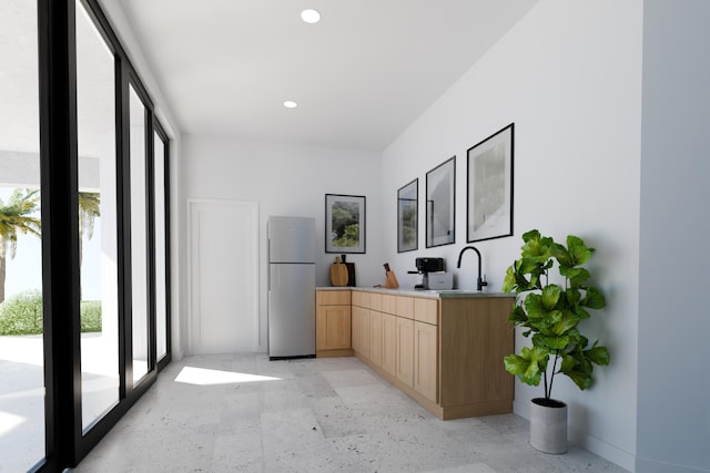 kitchen with light brown cabinetry, a sink, expansive windows, freestanding refrigerator, and recessed lighting