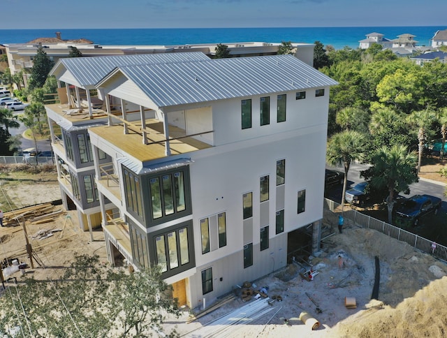 back of property featuring stucco siding, metal roof, fence, and a water view