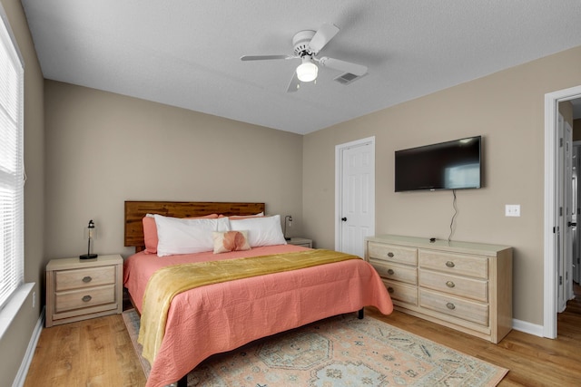 bedroom with a textured ceiling, light wood-style flooring, a ceiling fan, visible vents, and baseboards