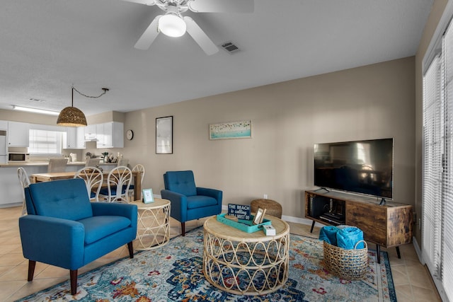 living area with light tile patterned floors, a ceiling fan, visible vents, and baseboards