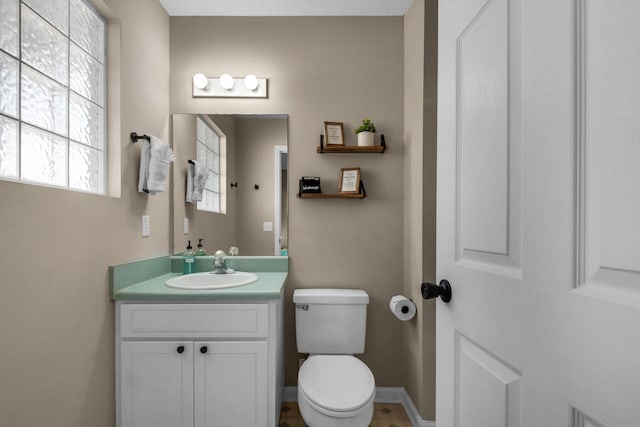 half bath with toilet, baseboards, and vanity