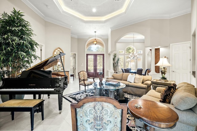 living area with a tray ceiling, french doors, crown molding, an inviting chandelier, and ornate columns