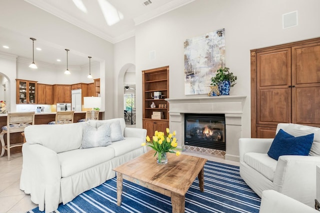 living room featuring arched walkways, a high ceiling, ornamental molding, a fireplace with flush hearth, and light tile patterned flooring