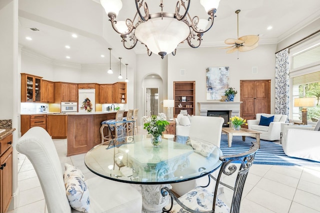 dining area featuring arched walkways, a high ceiling, crown molding, a fireplace, and light tile patterned flooring