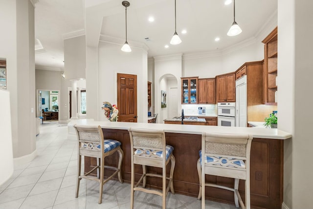 kitchen featuring brown cabinets, light tile patterned floors, double oven, ornamental molding, and glass insert cabinets