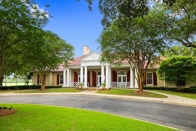 greek revival inspired property featuring a front yard, a chimney, a porch, and stucco siding