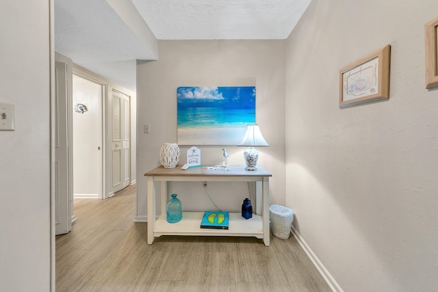 corridor with a textured ceiling, wood finished floors, and baseboards