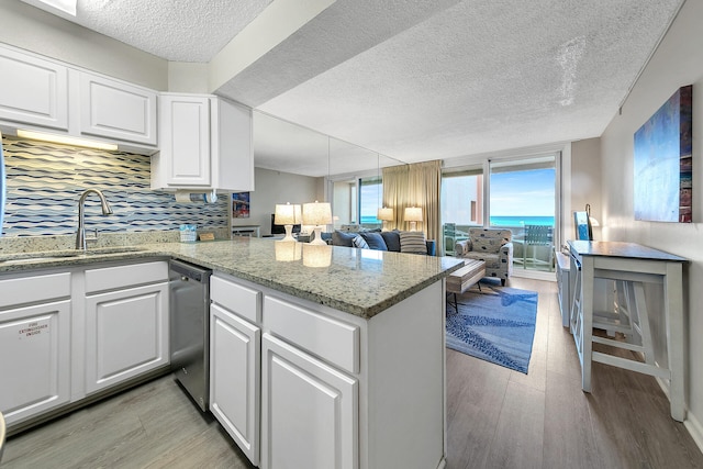 kitchen featuring a peninsula, a sink, open floor plan, stainless steel dishwasher, and light wood finished floors