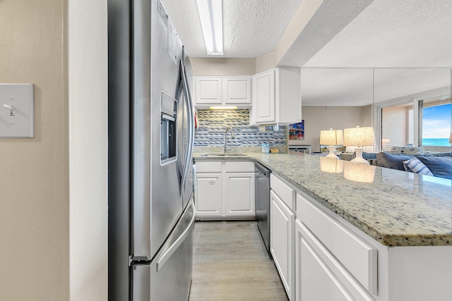 kitchen featuring light wood finished floors, white cabinets, a peninsula, stainless steel appliances, and a sink