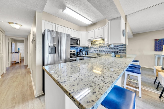 kitchen with light stone counters, stainless steel appliances, white cabinetry, light wood-type flooring, and a peninsula