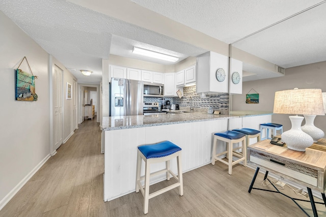 kitchen with stainless steel appliances, a peninsula, backsplash, and light wood-style floors