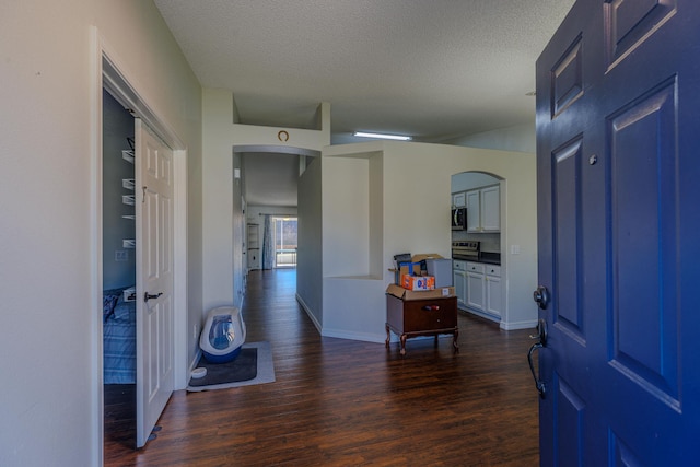 corridor with dark wood-style floors, a textured ceiling, arched walkways, and baseboards