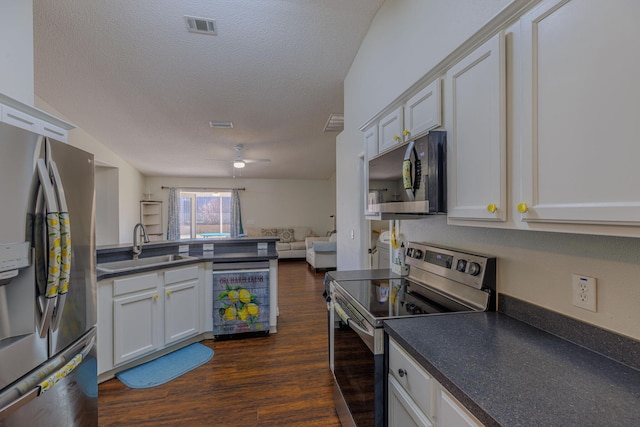 kitchen with dark wood finished floors, stainless steel appliances, dark countertops, open floor plan, and a sink