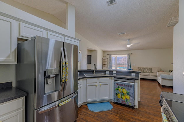 kitchen featuring stainless steel fridge with ice dispenser, dark countertops, dishwashing machine, open floor plan, and a sink