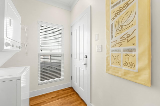 doorway with stacked washer and clothes dryer, light wood-style flooring, and baseboards