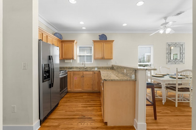 kitchen featuring light wood finished floors, appliances with stainless steel finishes, a peninsula, a kitchen bar, and a sink