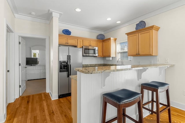 kitchen featuring a peninsula, stainless steel appliances, crown molding, light wood-style floors, and a kitchen bar