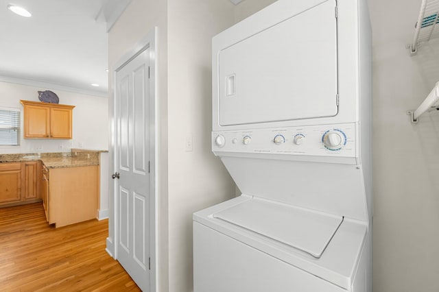 clothes washing area featuring stacked washer / dryer, laundry area, light wood-style flooring, and recessed lighting