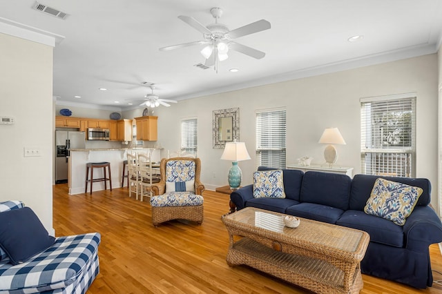 living area featuring ornamental molding, a wealth of natural light, visible vents, and light wood finished floors